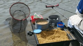 Fishing equipment, smack, food, red and white worms in the boxes on the holder, lake water in the background, no color grading, raw video.