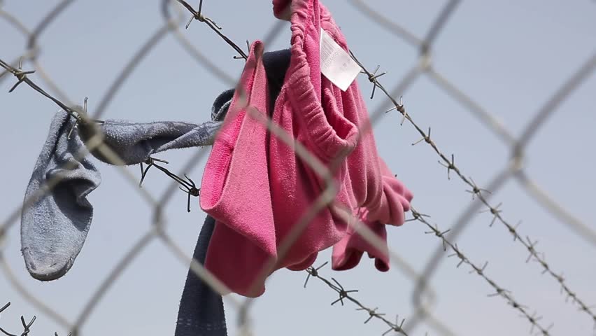 Children clothes hang on a razor wire fance meant to keep refugees out.