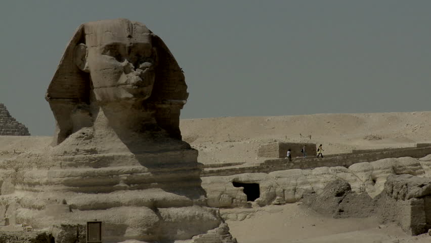 Long shot of head of Great Sphinx, tourist walking on base.
