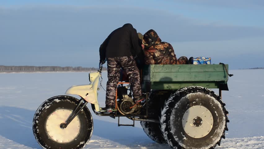 Two men trying to make a homemade motorcycle on the ice in winter the sea and the girl looks at them in a Blizzard.