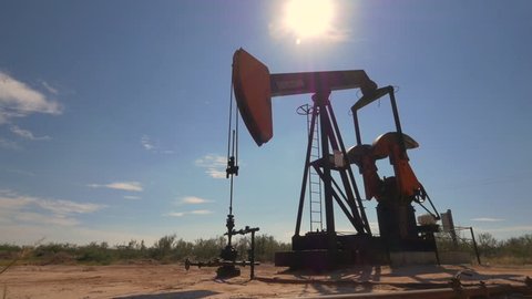 CLOSE UP: Industrial oil pump jack working and pumping crude oil for fossil fuel energy with drilling rig in oil field. Nodding donkey pump against the blue sky pumping over the sun in sunny summer