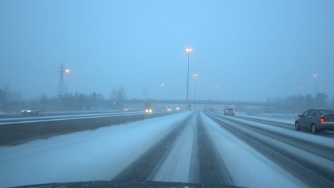 Driving down snow covered highway at rush hour in Canada. Speeding down a hazardous snowy freeway avoiding a crash. Wipers against snowfall on the dangerous road. High speed on slippery road.