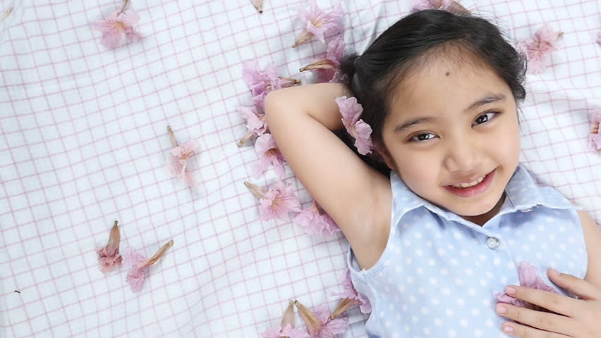 Little Asian child laying down on the floor with falling flowers, Slow motion shot