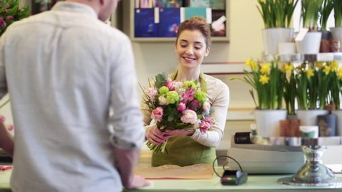 people, shopping, sale, floristry and consumerism concept - happy florist woman wrapping flowers in paper and man at flower shop