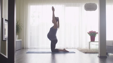Young Pregnant Woman Doing Stretching and Fitness in Living Room at Home. Shot on RED Cinema Camera.
