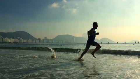 Athletic man running in slow motion through the waves on Copacabana Beach in Rio de Janeiro, Brazil