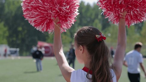 American dancing girl or teenager supports football team. Playing young novice athletes or professional players. Group in white T-shirt and short red skirt. Regular training and love of life. Close up