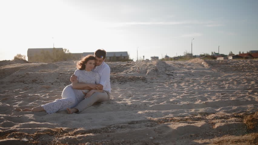 Young european couple sit on the sand on the seashore.Two people man and woman enjoy each other.man embrace his woman. Touch her hands.