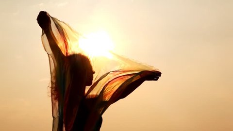 woman against sky and sun has hold thin shawl which waves on wind