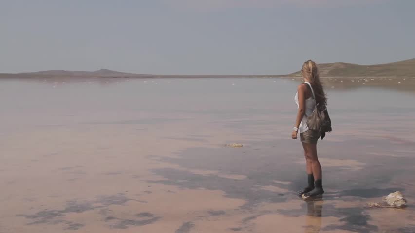 View of deserted salt lake with foot print in the foreground and young attractive woman with long blonde hair standing on a rock and looking  into the distance.Koyashskoye lake, Crimea, Ukraine.