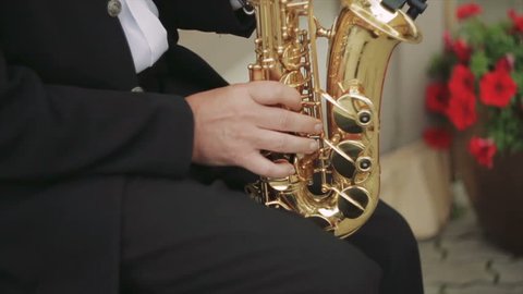 Close-Up on Fingers Pressing the Keys of the Instrument. Musician Playing the Saxophone in the Street. the Camera Moves Up. in Fixed Wireless Microphone Saxophone. a Man in a Black Suit and White