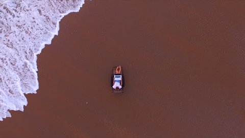 Top view of aerial shooting from flying drone of hipster girl is chatting with friends in social network via net-book by using global internet, while is relaxing on a beach near ocean with calm waves
