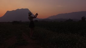 Aerial shooting from drone of a woman wanderer is taking photo with cellphone camera, while is standing in Thailand rural against silhouette of high mountains during her long-awaited vacation abroad