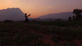 Aerial shooting from flying drone of a young hipster girl is making photo with mobile phone camera of a beautiful scenery of Thailand, while is standing against mountains  silhouette and evening sky
