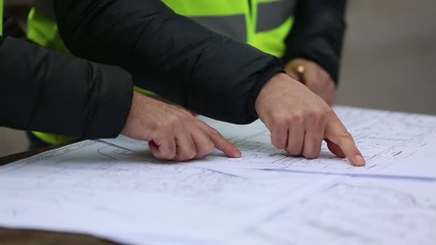 Hands of construction personnel with office blueprints