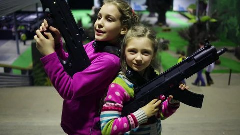 Two girls pose together with machine guns near stairs