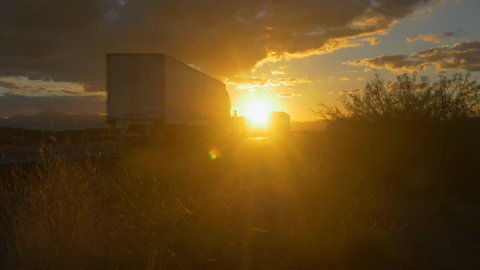 4K CLOSE UP: Personal cars and big freight transporting semi trucks driving on busy highway at beautiful golden sunset in summer. Traffic on busy freeway speeding over the setting sun.