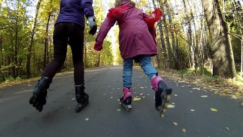 Back of woman and girl roller skating in autumn park at sunny day, action camera