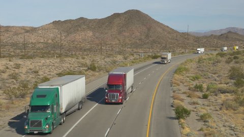 4K AERIAL SLOW MOTION CLOSE UP: Cars and trucks driving on busy highway through the desert. Freight semi trucks transporting goods, personal cars on a road trip, people traveling in sunny summer