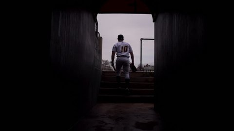 Slow motion wide shot of baseball player walking to field in tunnel