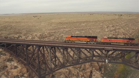 AERIAL: Container freight train crossing steel arch railroad bridge across the Canyon Diablo in the middle of the vast desert in Arizona. Rail freight transport delivering goods