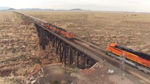 AERIAL: Two container freight trains crossing steel arch railroad bridge across the Canyon Diablo in the middle of the vast desert in Arizona. Rail freight transport delivering goods