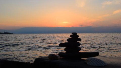 Zen stones pyramide on the beach at background of sunset. View from the Fiesa beach on the Adriatic coast of Slovenia, Piran city at background.