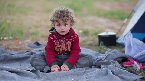 Idomeni, Greece - April 17, 2016: A refugee child spends the evening outside a tent in an improvised camp where over ten thousand people are waiting.