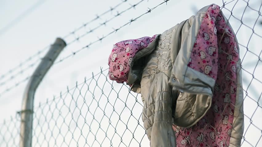 A child's jacket hangs on a razor wire fence erected to keep immigrants away. Royalty-Free Stock Footage #15966955