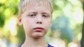 Close up portrait of sad unhappy 8 years old boy over green trees background. Cute face of little blond kid isolated at nature background.8 years old boy. Real time video footage