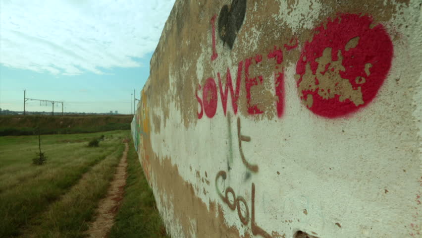 Locked off shot of a man walking alongside a wall in Soweto
