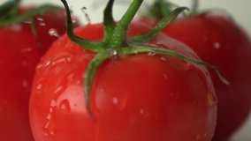 Multiple water drops hit fresh red ripe tomato with green leaves super slow motion video