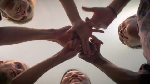 A group of 5 young millennials do an exploding fist bump with their hands together in the center of a circle and then cheer in a celebration of a successful event - low angle shot.