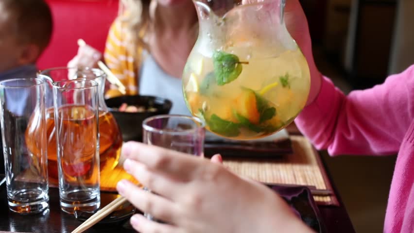 Girl in pink pouring lemonade from carafe into glass at table in sushi restaurant.