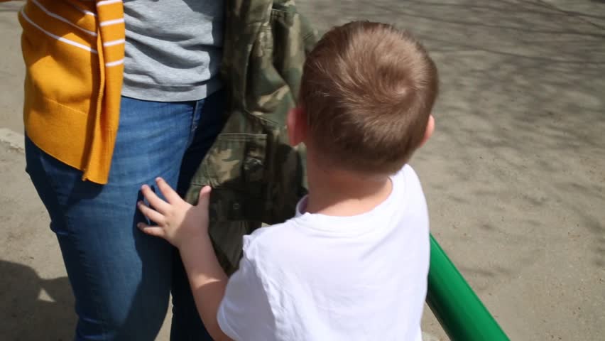 Little boy crying and grasping his mothers hands on street.