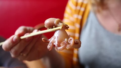 Woman with chinese chopsticks putting small octopus in mouth close up.