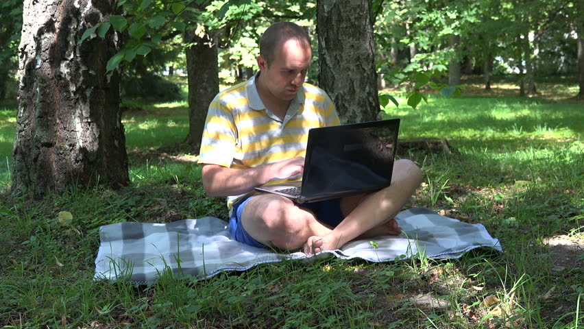 young man using laptop wifi technology in green nature park outdoor. video clip.