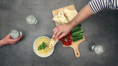 Preparing Hummus / Houmous - oriental recipe (stop motion animation). Top view on ingredients and timelapse of eating with pita bread and fresh vegetables.
