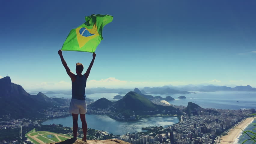 Athlete stands holding a Brazilian flag at a bright overlook of the city skyline of Rio de Janeiro, Brazil Royalty-Free Stock Footage #15984838