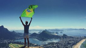 Athlete stands holding a Brazilian flag at a bright overlook of the city skyline of Rio de Janeiro, Brazil