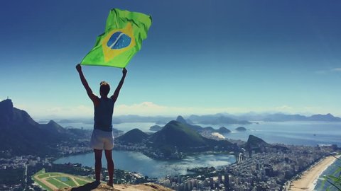 Athlete stands holding a Brazilian flag at a bright overlook of the city skyline of Rio de Janeiro, Brazil Stock Video