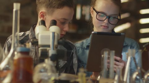 Young boy is making chemistry experiments while girl is looking at a tablet computer in a garage at home. Shot on RED Cinema Camera in 4K (UHD).