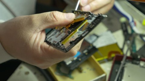 Footage of a man repairing a broken cell phone in a cell phone service...