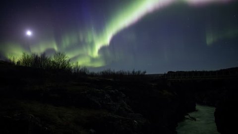 Strong winding aurora northern lights over volcanic lava field river moonlight trees pan Iceland 4k
