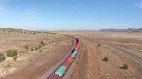 SELIGMAN ARIZONA USA, OCTOBER 20th 2015: AERIAL: Long container freight train with many cargo wagons transporting goods through the vast desert landscape across the country