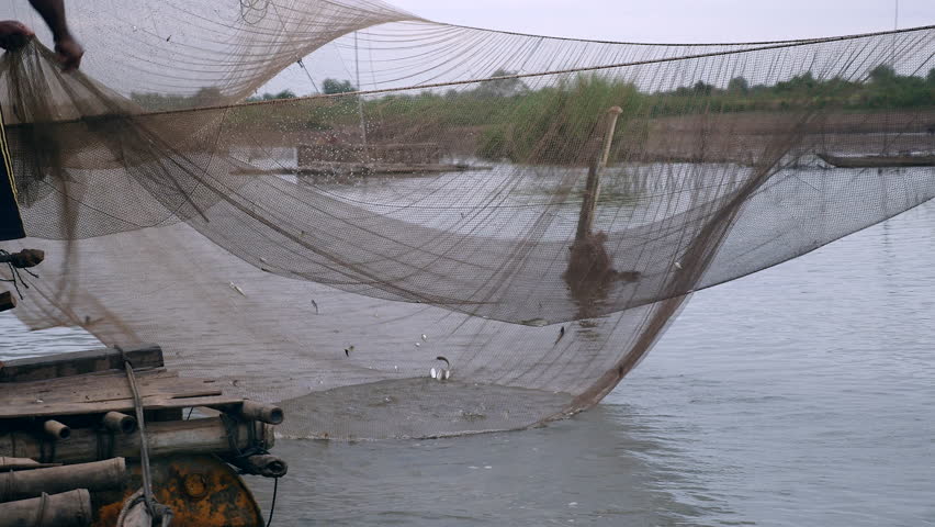 Water-level view on river chinese fishing net and fisherman using a hand net to catch fishes out of it