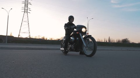 Young man sitting on motorcycle on the road at sunset, slow motion