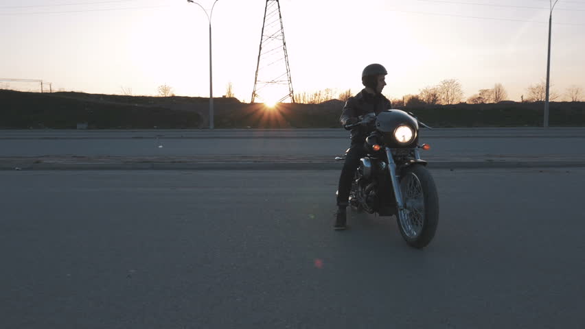 Young man sitting on motorcycle on the road at sunset, slow motion