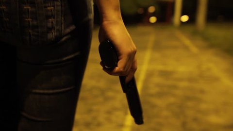A WOMAN WALKING WITH A GUN IN HER HAND