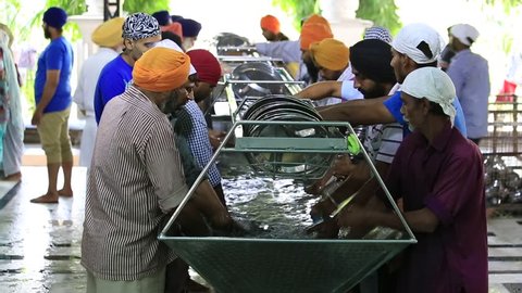 AMRITSAR, INDIA - SEPTEMBER 27, 2014: Unidentified poor indian people wash dishes at a soup kitchen in the Sikh Golden Temple